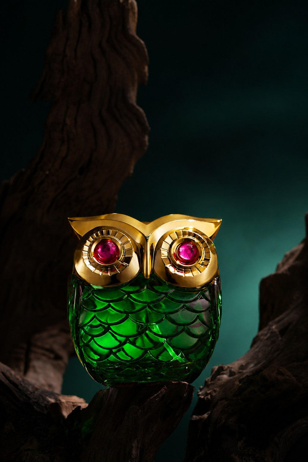 Owl-shaped fragrance bottle in emerald glass with a gold head, resting on dark wood